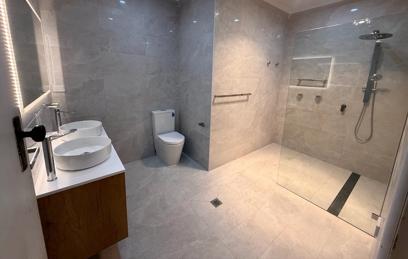 Modern renovated bathroom with stone-look tiles, twin basins and a walk-in shower by Quick Mick’s Plumbing